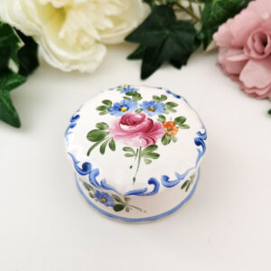 Boîte ronde en faïence blanche décorée à la main de fleurs bleues et roses, couvercle orné d’un motif central.