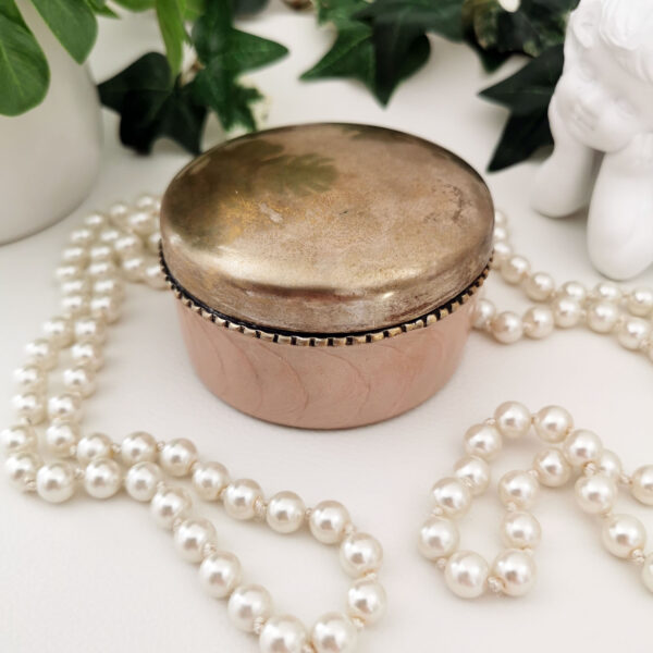 Boîte vintage ronde en métal doré et rose irisé, posée sur fond clair avec perles en décoration