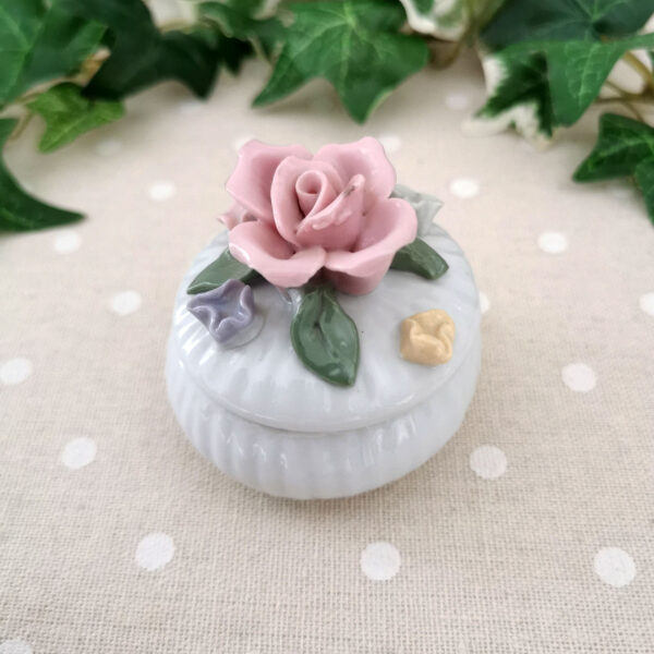 Mini-boîte ronde en porcelaine blanche décorée de fleurs pastel en relief, posée sur un tissu à pois.
