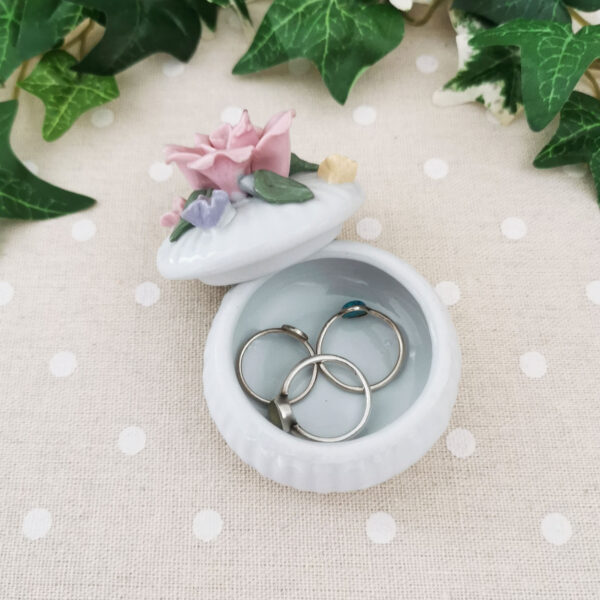 Mini-boîte ronde en porcelaine blanche décorée de fleurs pastel en relief, posée sur un tissu à pois.